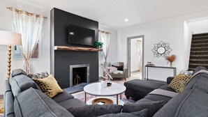 Una sala de estar moderna con chimenea, un sofá grande, una mesa de centro y un televisor montado en la pared.