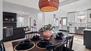 Un comedor moderno con una mesa redonda para cuatro personas, una lámpara colgante trenzada grande y una cocina al fondo.