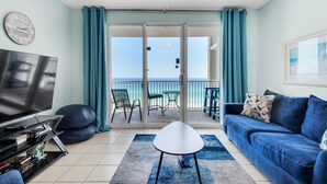 Sala de estar com televisão, sofá e vista para o oceano por uma porta deslizante.