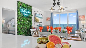 A modern living room with a view of the ocean, a fruit bowl on the counter, and a neon sign on the wall.