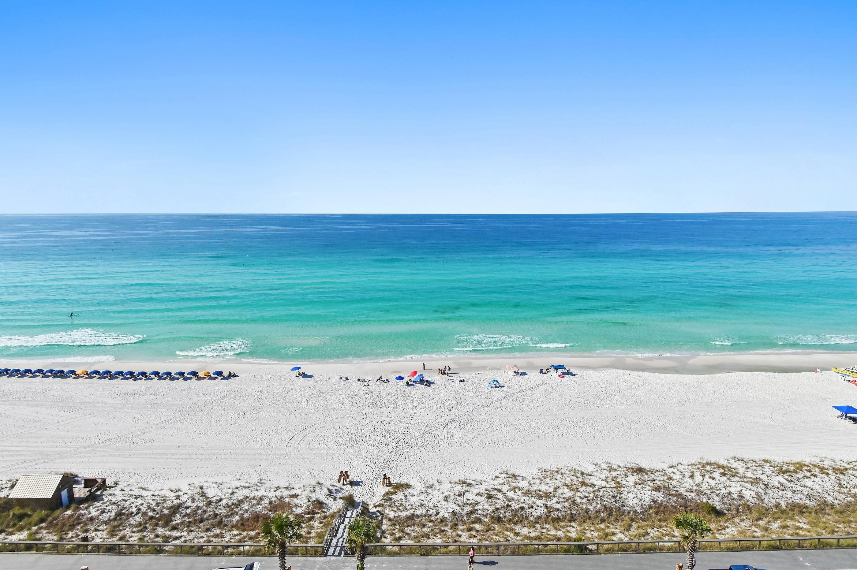 A beach with white sand, clear turquoise water, and umbrellas.