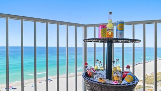 A balcony with a view of the beach, a wicker basket with drinks, and a railing.