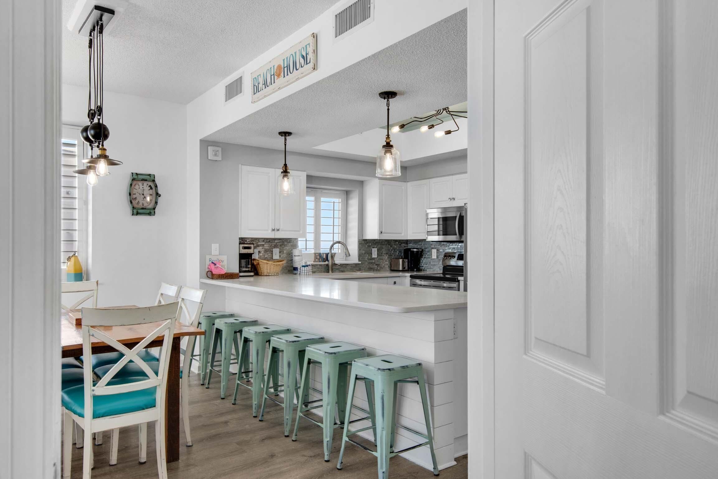 Una cocina moderna con armarios blancos, una isla grande con taburetes de bar, iluminación colgante y un reloj en la pared.