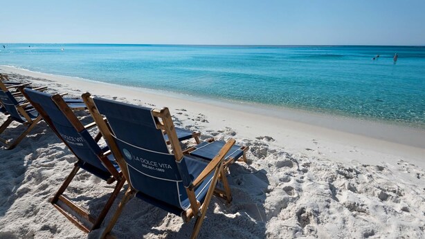 A beach with rows of blue lounge chairs and a clear view of the ocean. - Majestic Sun 1012a (Miramar Beach)