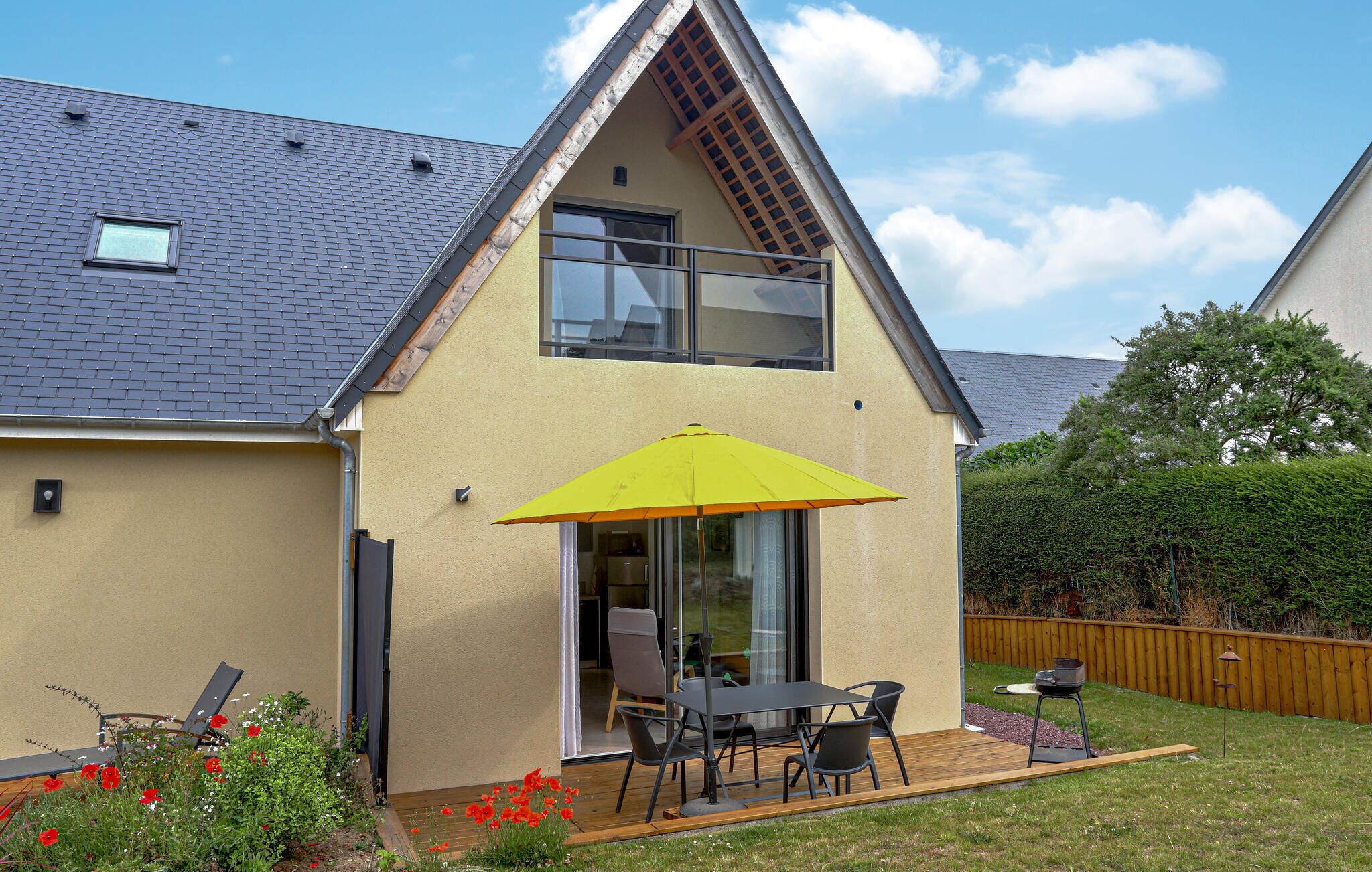 Una casa moderna con techo inclinado, un balcón con sombrilla amarilla y un patio con mobiliario exterior.