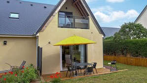 Ein modernes Haus mit Satteldach, einem Balkon mit gelbem Sonnenschirm und einer Terrasse mit Gartenmöbeln.