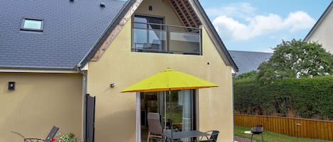 Et moderne hus med skråt tag, en balkon med gul parasol og en terrasse med udendørs møbler.