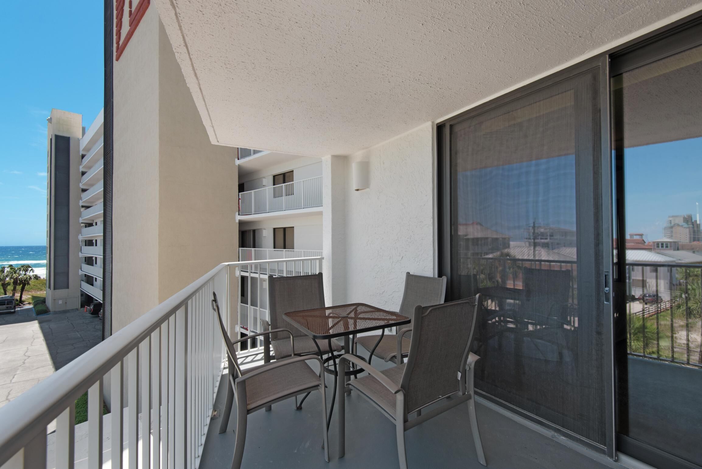 A balcony with a table and chairs, overlooking a building with multiple balconies and a view of the ocean.