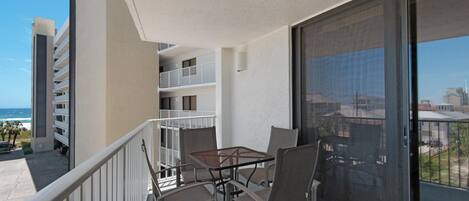 A balcony with a table and chairs, overlooking a building with multiple balconies and a view of the ocean.