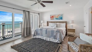 Une chambre avec un lit, un ventilateur de plafond, une table de chevet, une lampe, une vue sur la plage et un balcon.