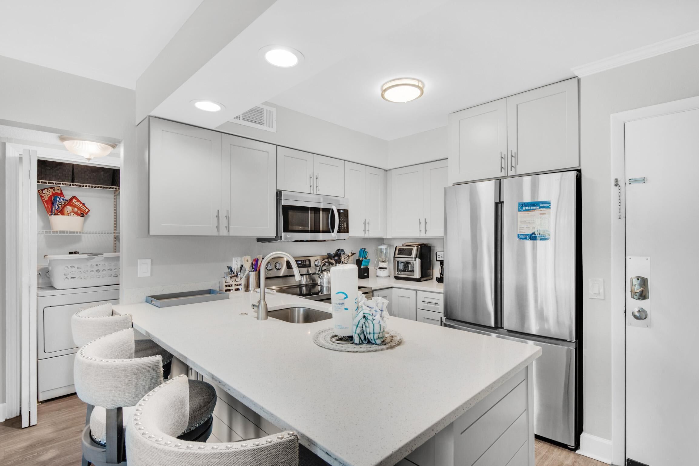 A modern kitchen with white cabinetry, stainless steel appliances, and a central island with bar stools.