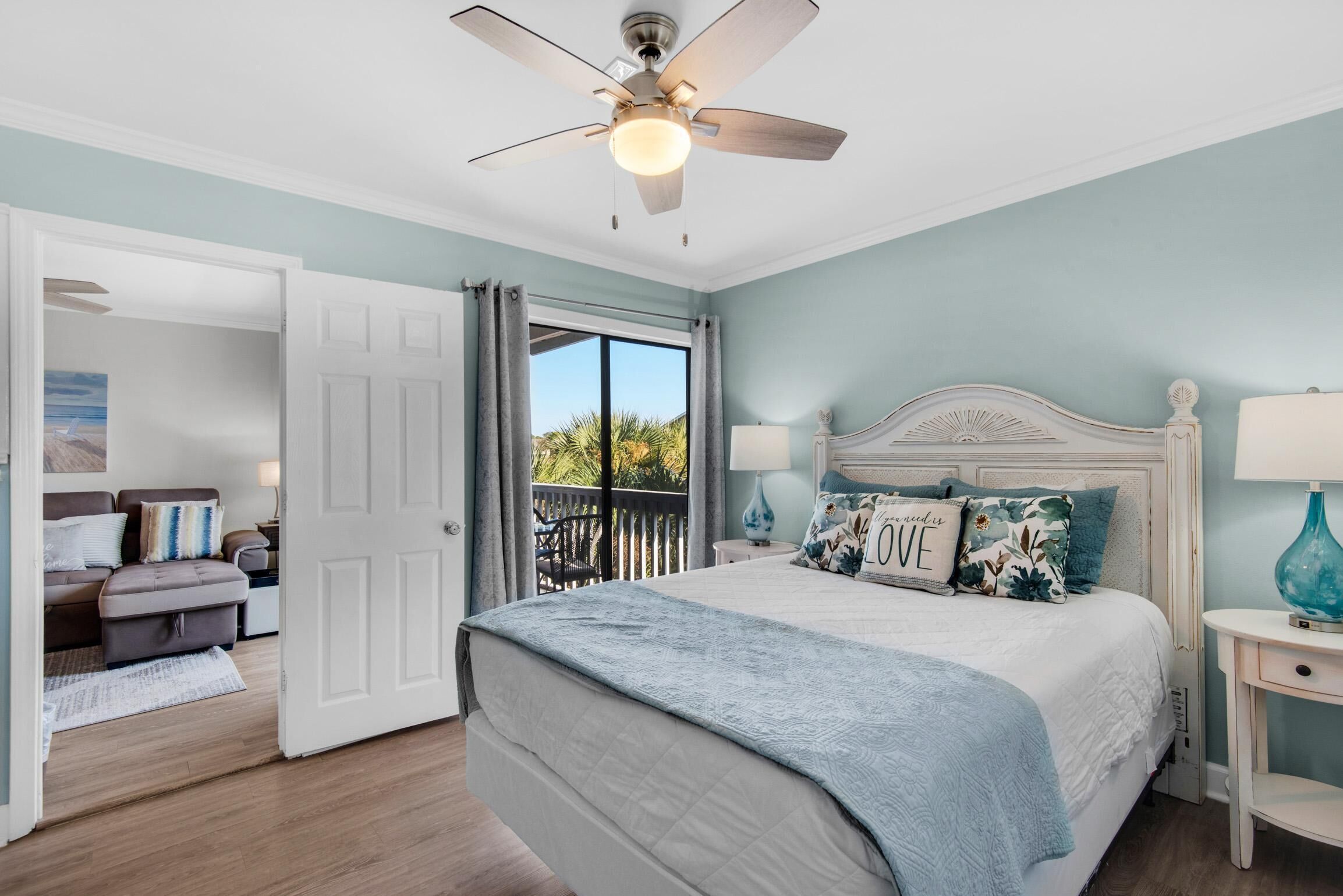 A bedroom with a bed, a ceiling fan, a nightstand, and a view of the outdoors.