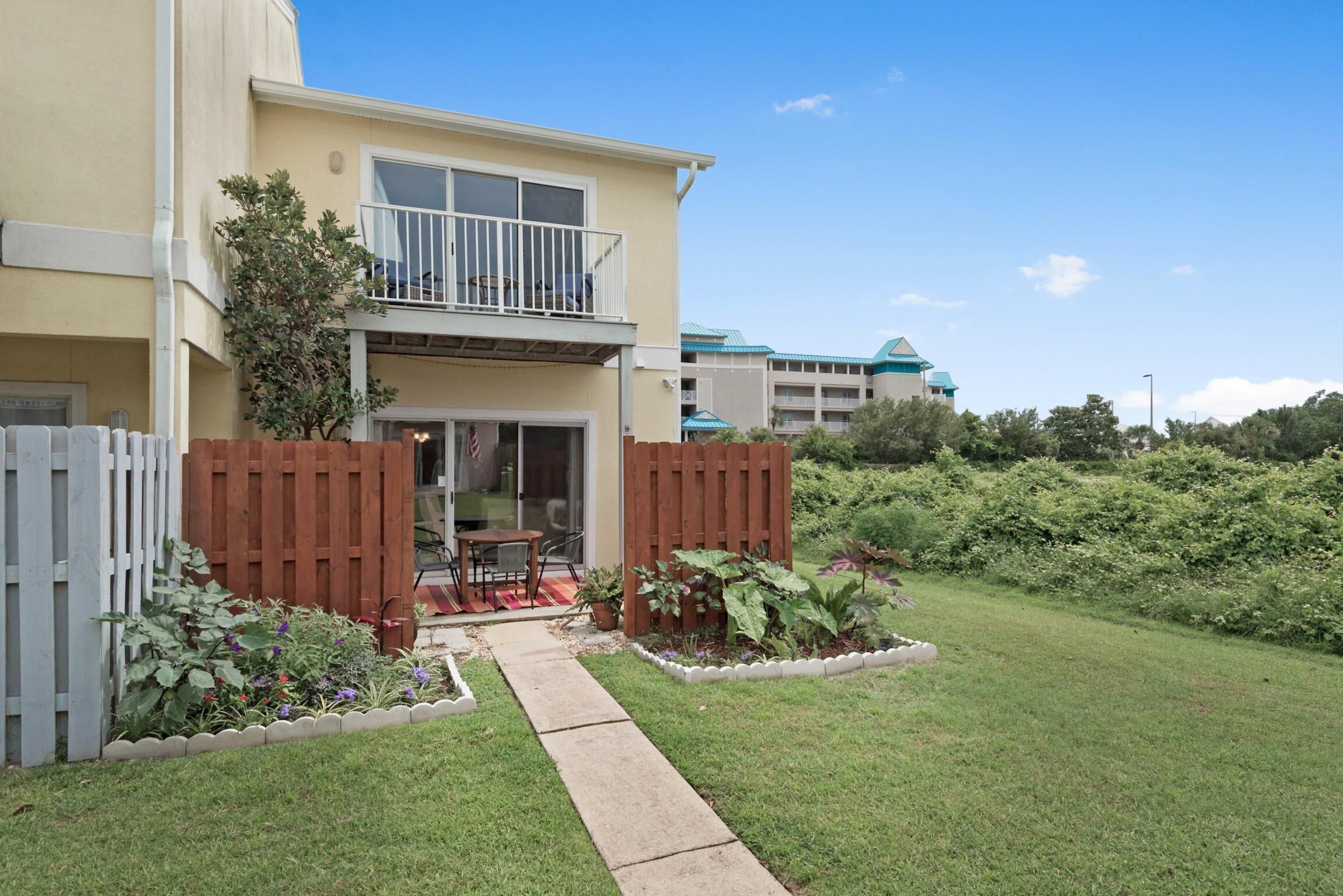 A two-story building with a balcony, a small patio with outdoor furniture, and a well-maintained garden.
