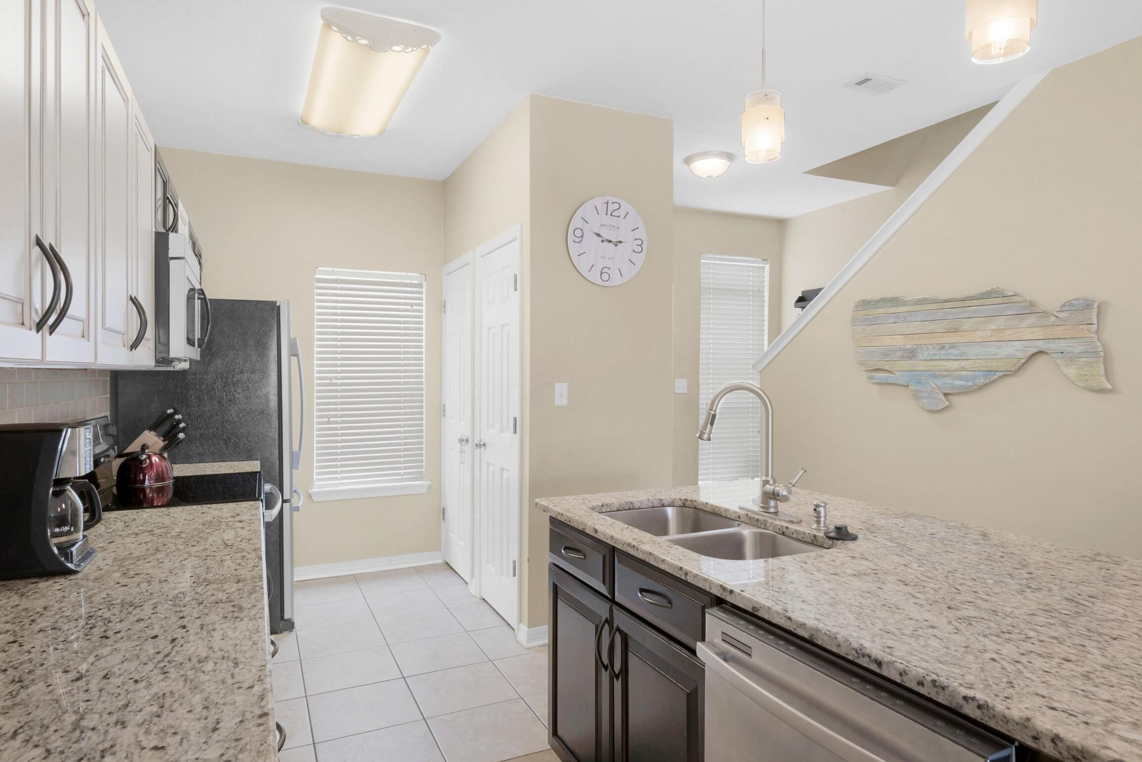 A kitchen with granite countertops, stainless steel appliances, and a clock on the wall.
