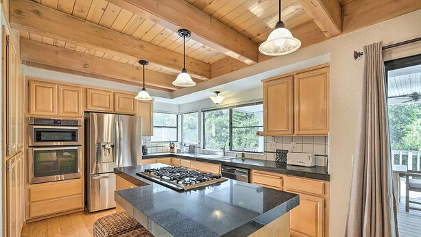 A spacious kitchen with wooden cabinets, a central island, stainless steel appliances, and pendant lighting. - NEW Winter Retreat 4B Hot Tub Sauna Pets Welcome with Tranquil Creek in Backyard (Auburn)