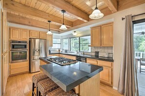 A spacious kitchen with wooden cabinets, a central island, stainless steel appliances, and pendant lighting. - NEW Winter Retreat 4B Hot Tub Sauna Pets Welcome with Tranquil Creek in Backyard (Auburn)