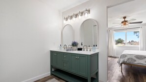 Une salle de bain avec un meuble-lavabo, deux miroirs, un ventilateur de plafond et une fenêtre donnant sur un beau paysage.