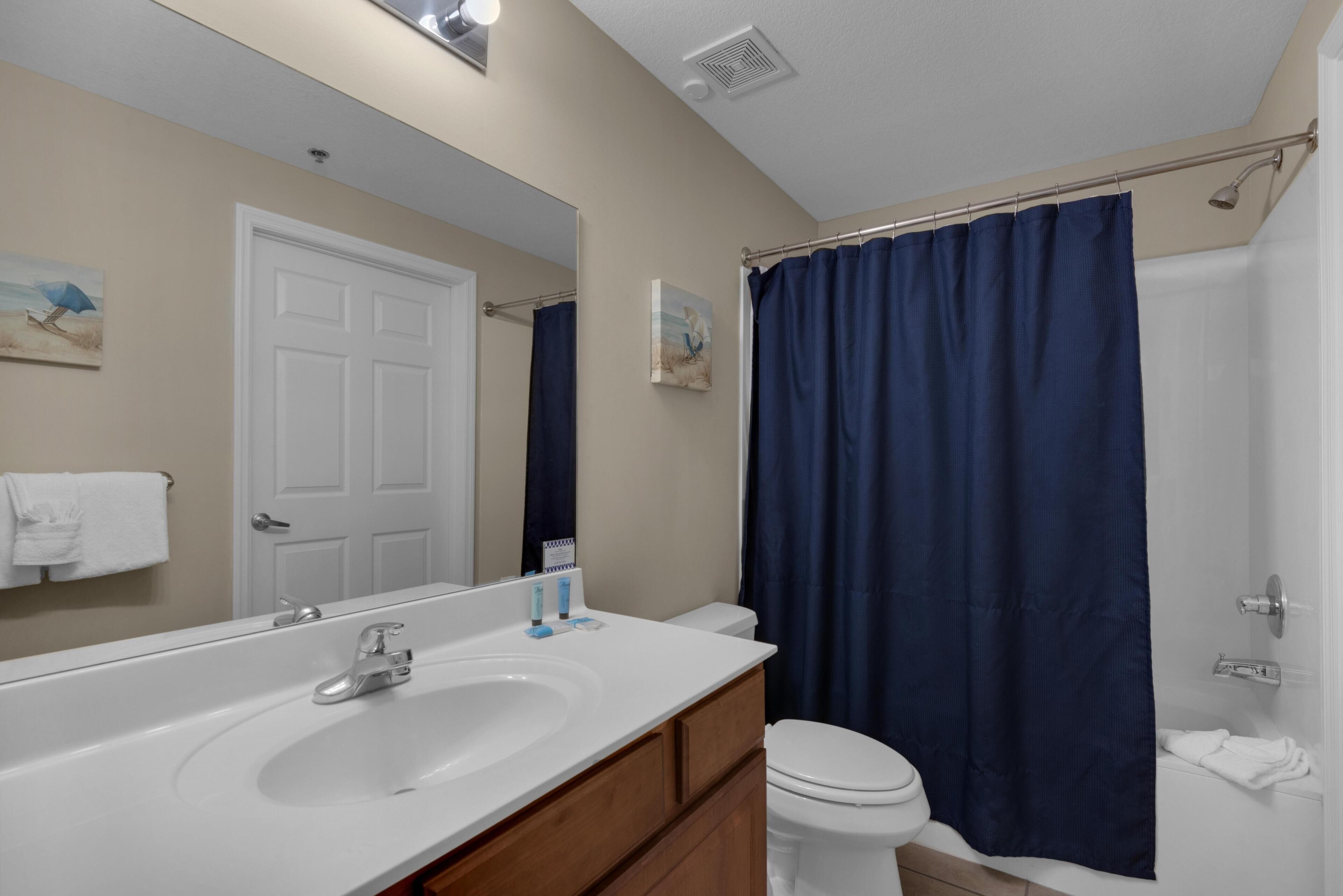 Une salle de bain avec un lavabo blanc, des toilettes, un rideau de douche et un miroir.