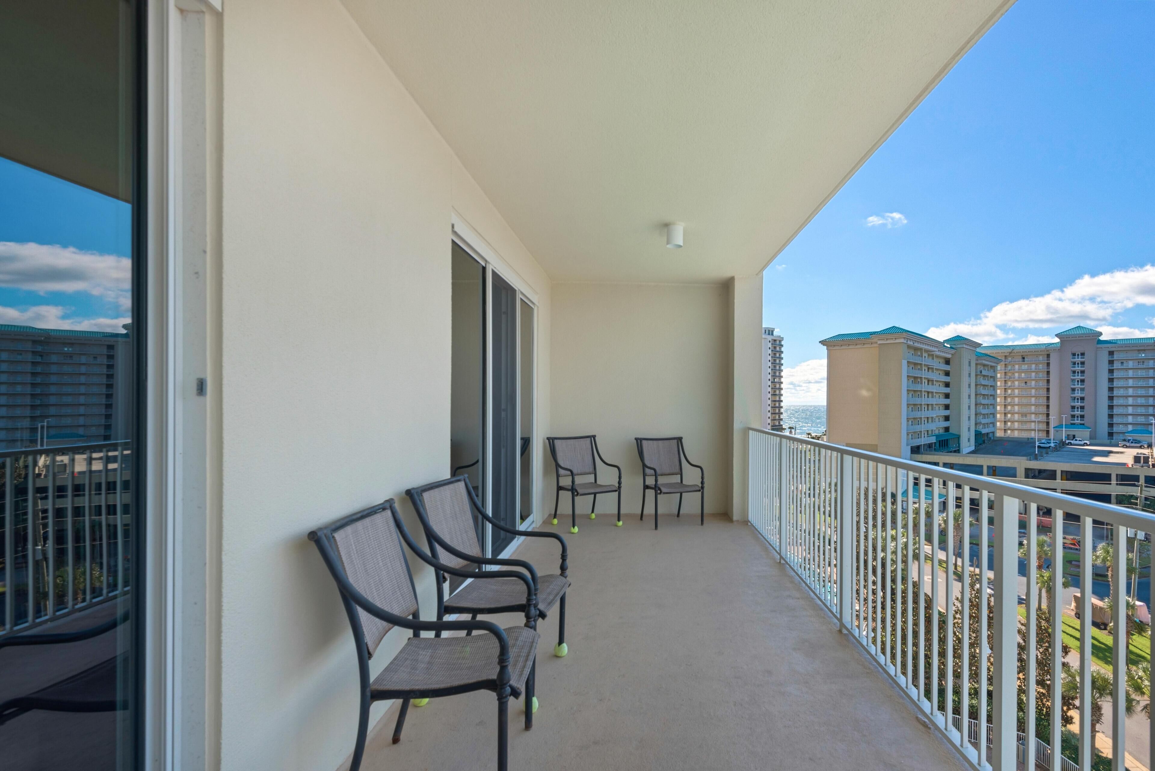 A balcony with four chairs, a glass door, and a view of other buildings.