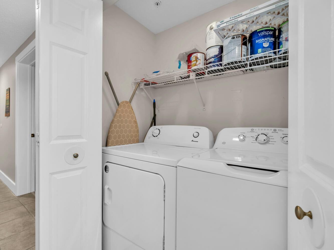 A laundry room with a washer and dryer, a mop, and a shelf with cleaning supplies.
