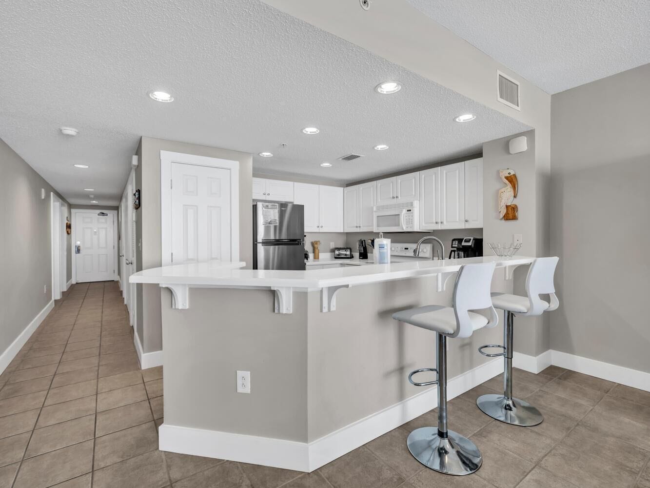 A modern kitchen with white cabinetry, a central island with bar stools, and a stainless steel refrigerator.