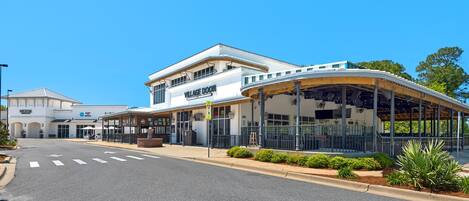 A modern building with a curved glass facade, a sign reading "VILLAGE DOOR," and a covered outdoor seating area.