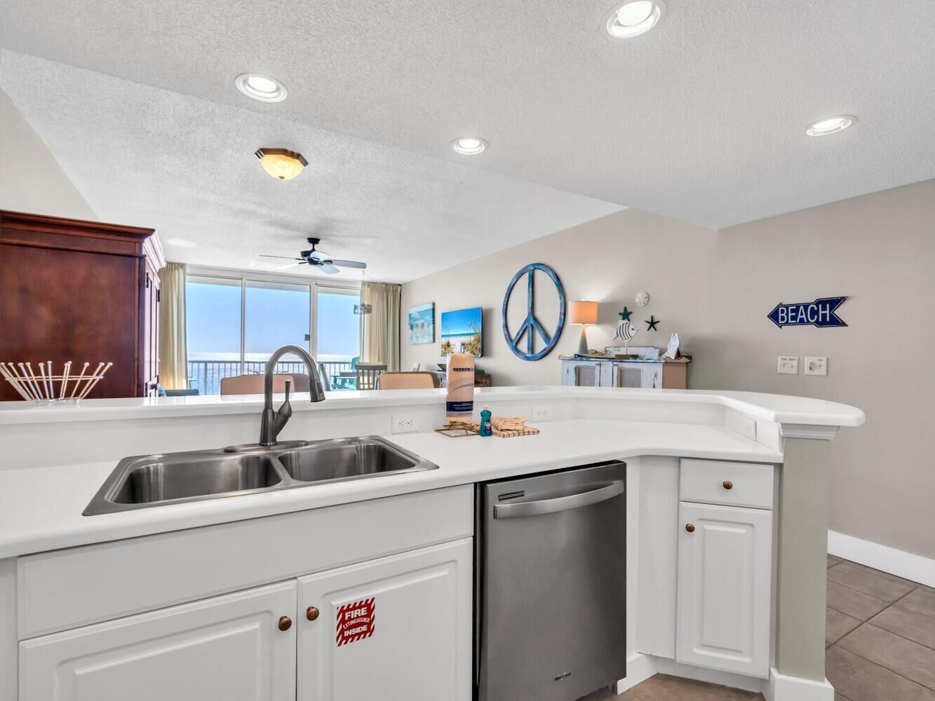 A modern kitchen with a stainless steel sink, white cabinetry, and a dishwasher. There is a large window providing a view of the outdoors.