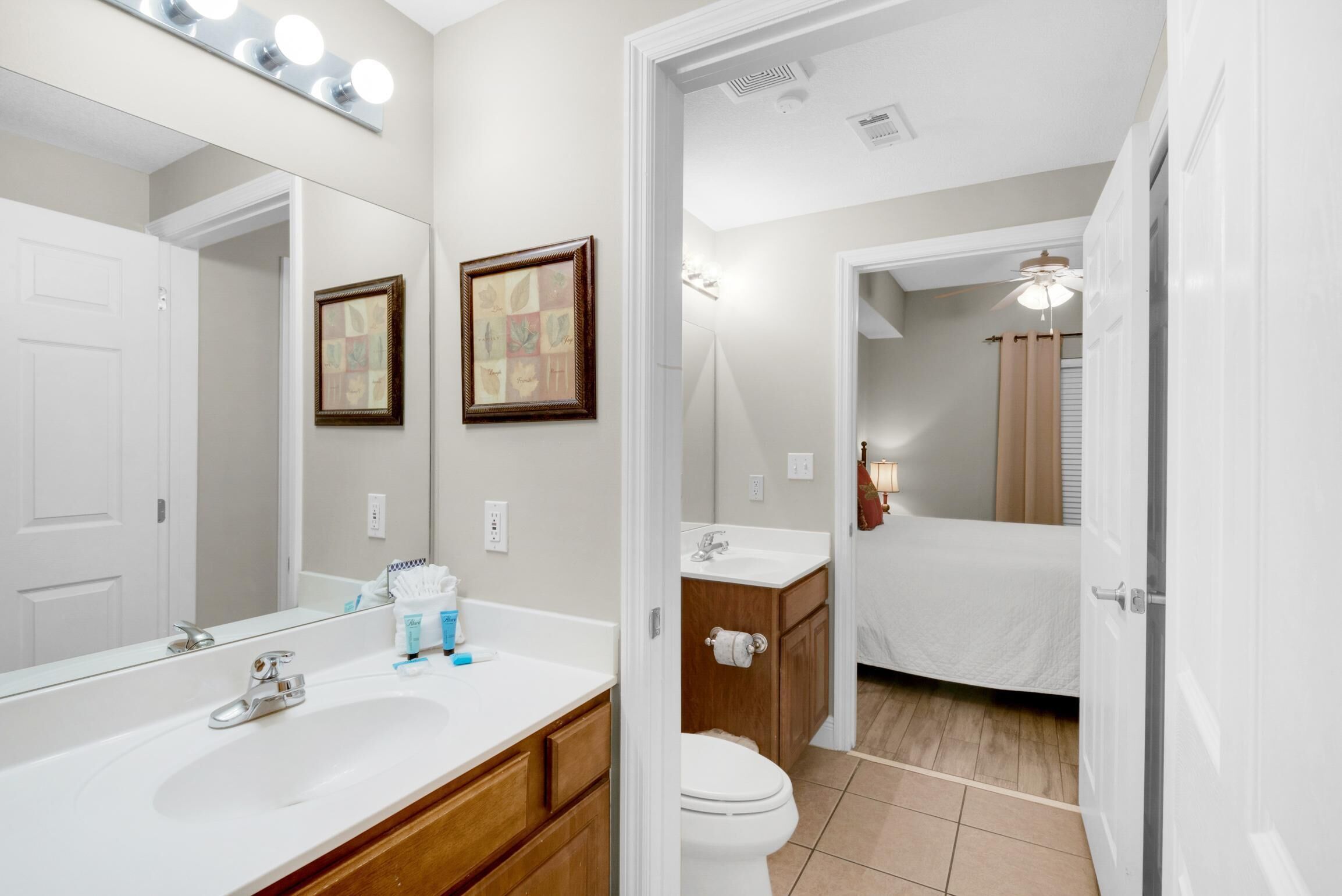 A bathroom with a white sink, mirror, and toilet. There are framed pictures on the wall and a ceiling light fixture.