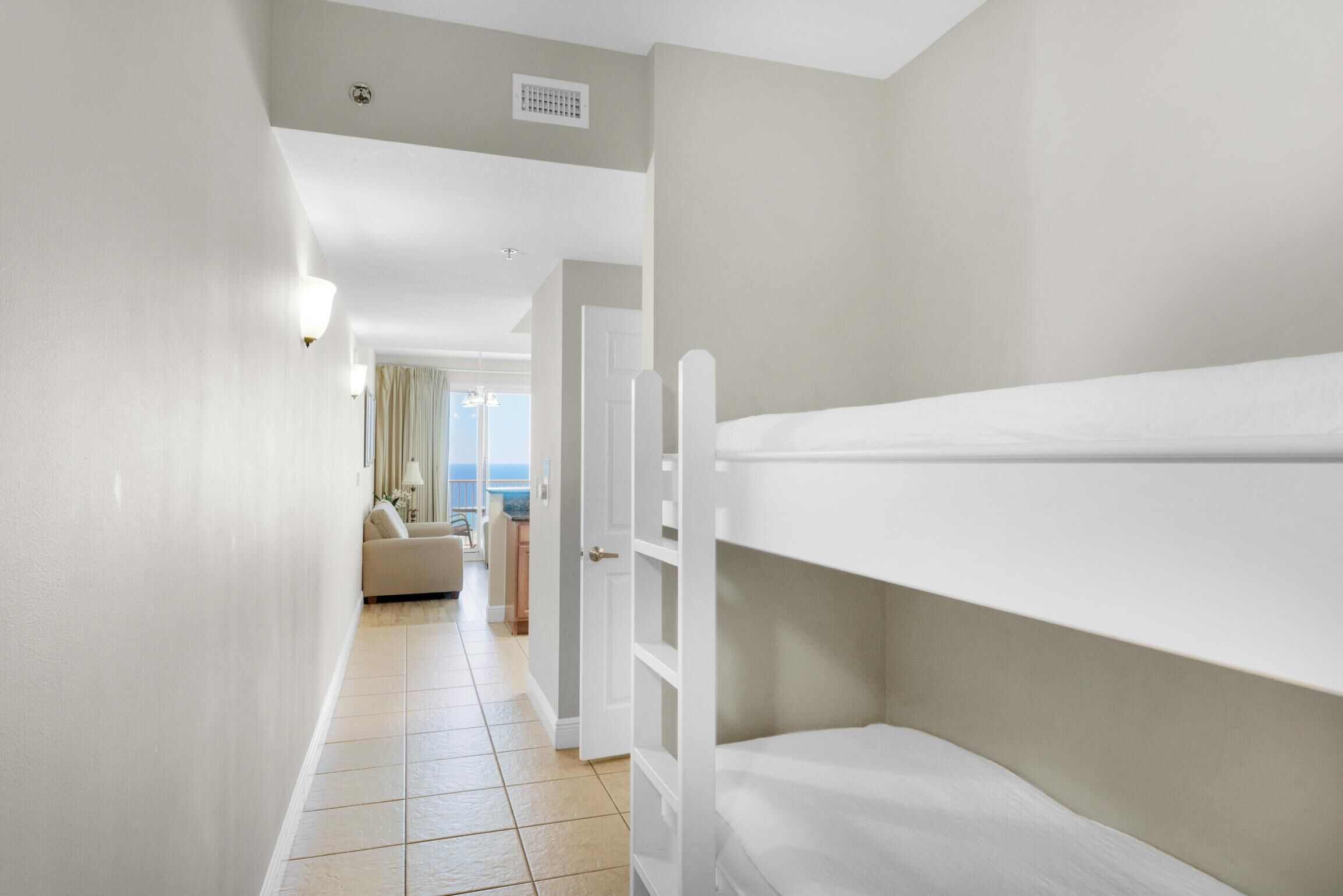 Een hotelkamer met stapelbedden, een gang die leidt naar een zithoek met een bank en uitzicht op zee.