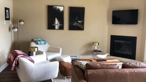 Ein modernes Wohnzimmer mit einer Couch, einem Sessel und einem an der Wand befestigten Flachbildfernseher.