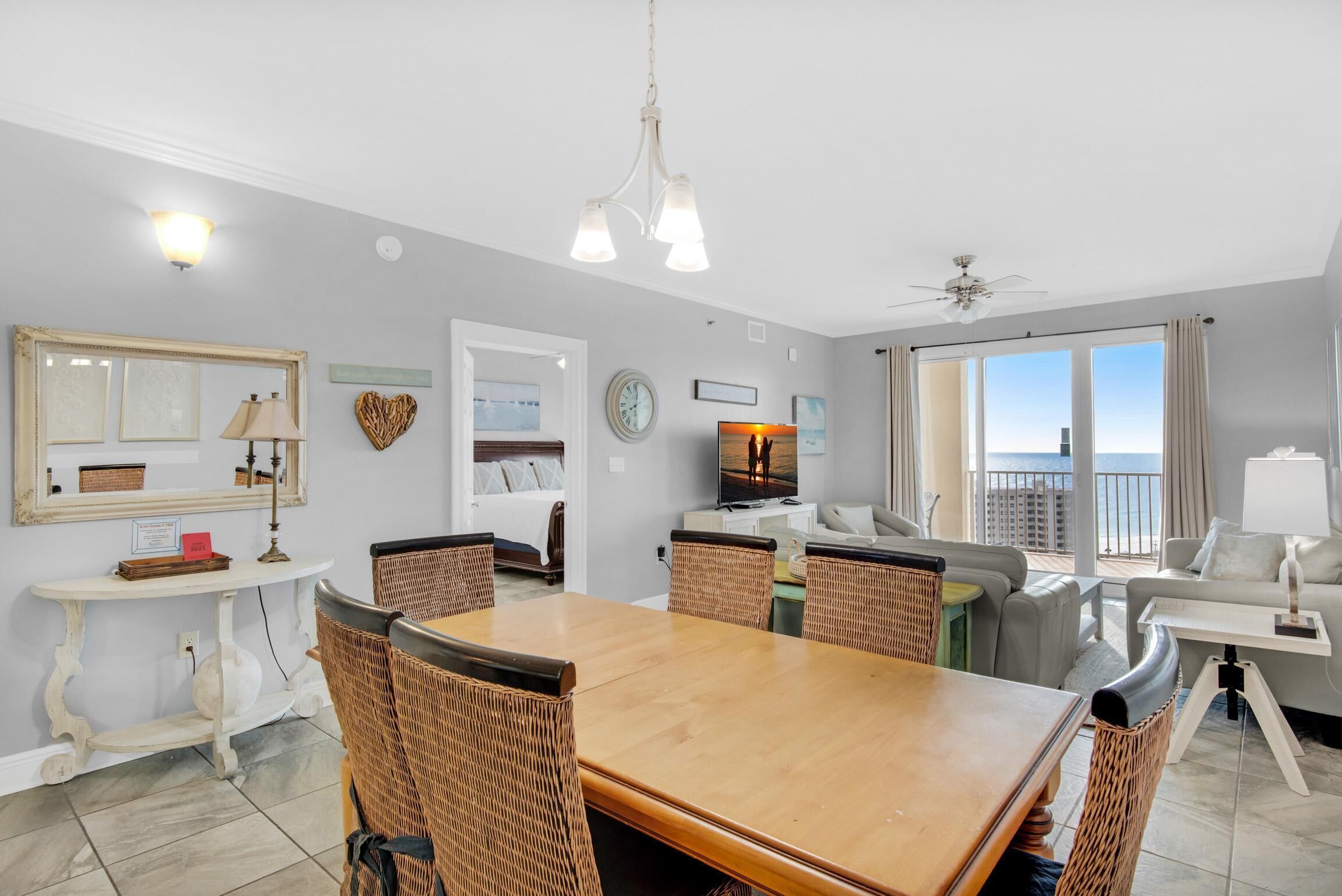 A spacious living area with a dining table, wicker chairs, a sofa, and a balcony with a view.