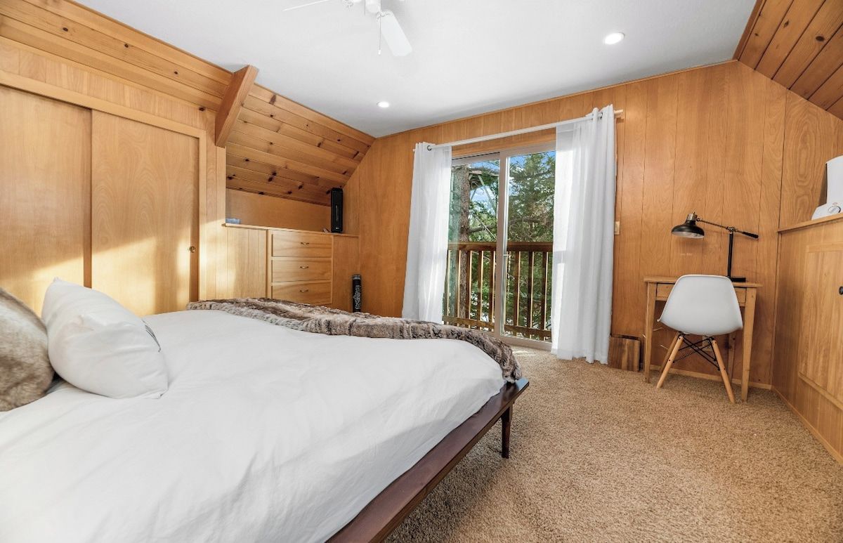 Une chambre à coucher comprenant un lit, un bureau, une chaise, un ventilateur de plafond et une fenêtre avec des rideaux.