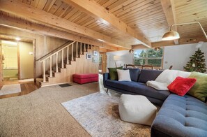 A spacious living room with a wooden staircase, a dark-colored sofa set, and a Christmas tree.