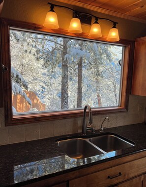 A kitchen with a large window, a double sink, and three pendant lights.