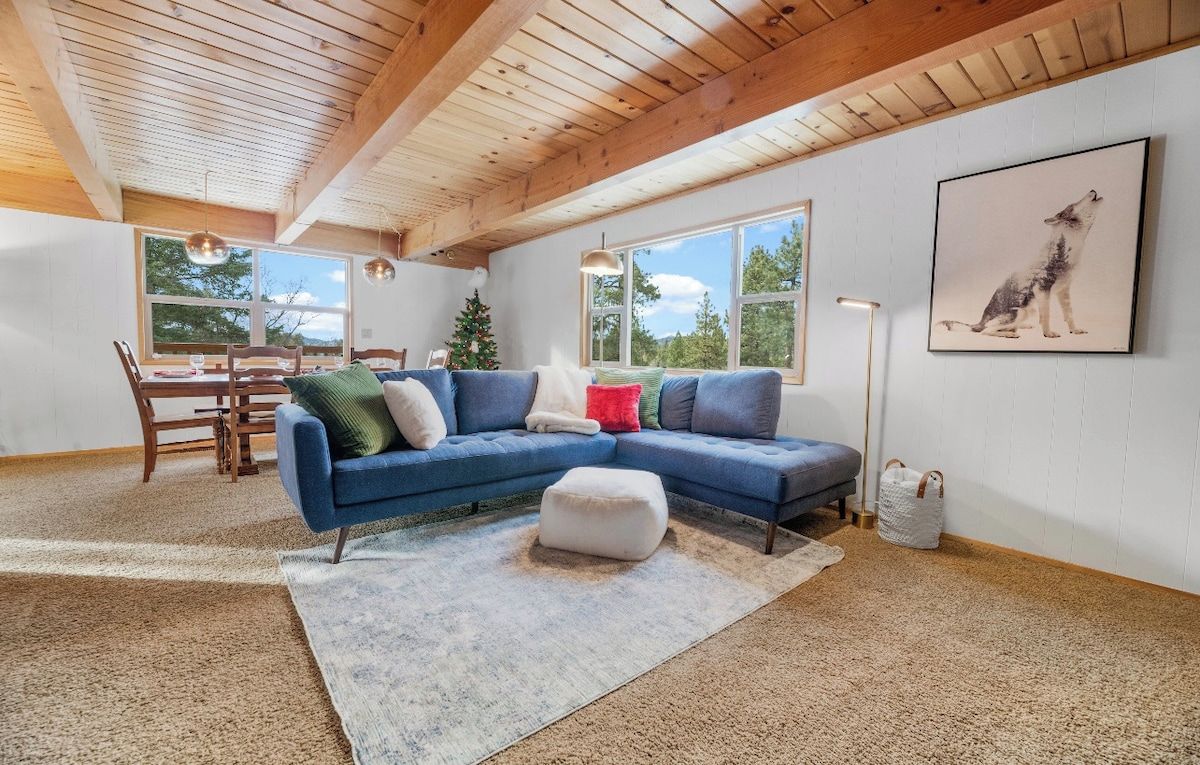 A spacious living room with a blue sectional sofa, a dining table, and a Christmas tree.