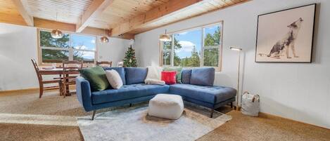 A spacious living room with a blue sectional sofa, a dining table, and a Christmas tree.
