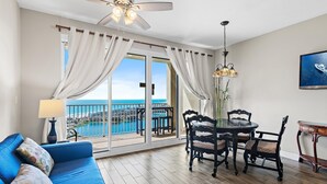 Uma varanda com vista para o mar, um sofá azul, uma mesa de jantar com cadeiras e um ventilador de teto.