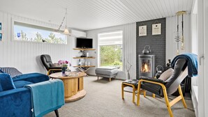 A cozy living room with a fireplace, comfortable seating, a flat-screen TV, and a large window offering a view of greenery. - 3 bedroom awesome home in Ulfborg (Ulfborg)