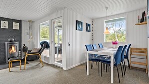 A cozy room with a fireplace, a dining table with chairs, and a view of the outdoors. - 3 bedroom awesome home in Ulfborg (Ulfborg)