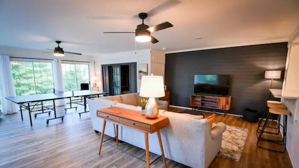 A modern living room with a sofa, coffee table, TV, and ceiling fans. - Spacious, Town Square, Theatre Room! 4 bed / 2 bath Private Home on town square (Covington)