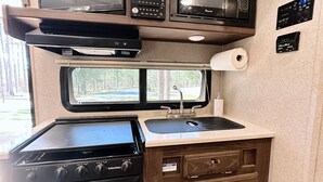 A compact RV kitchen with a stove, microwave, and a small window. - Joy ~ The Happy Little Camper (Loranger)