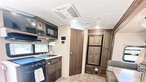 A compact RV kitchen with a stove, microwave, and sink. - Joy ~ The Happy Little Camper (Loranger)