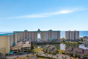 A large hotel with a central archway, multiple parking lots, and a body of water in the foreground.