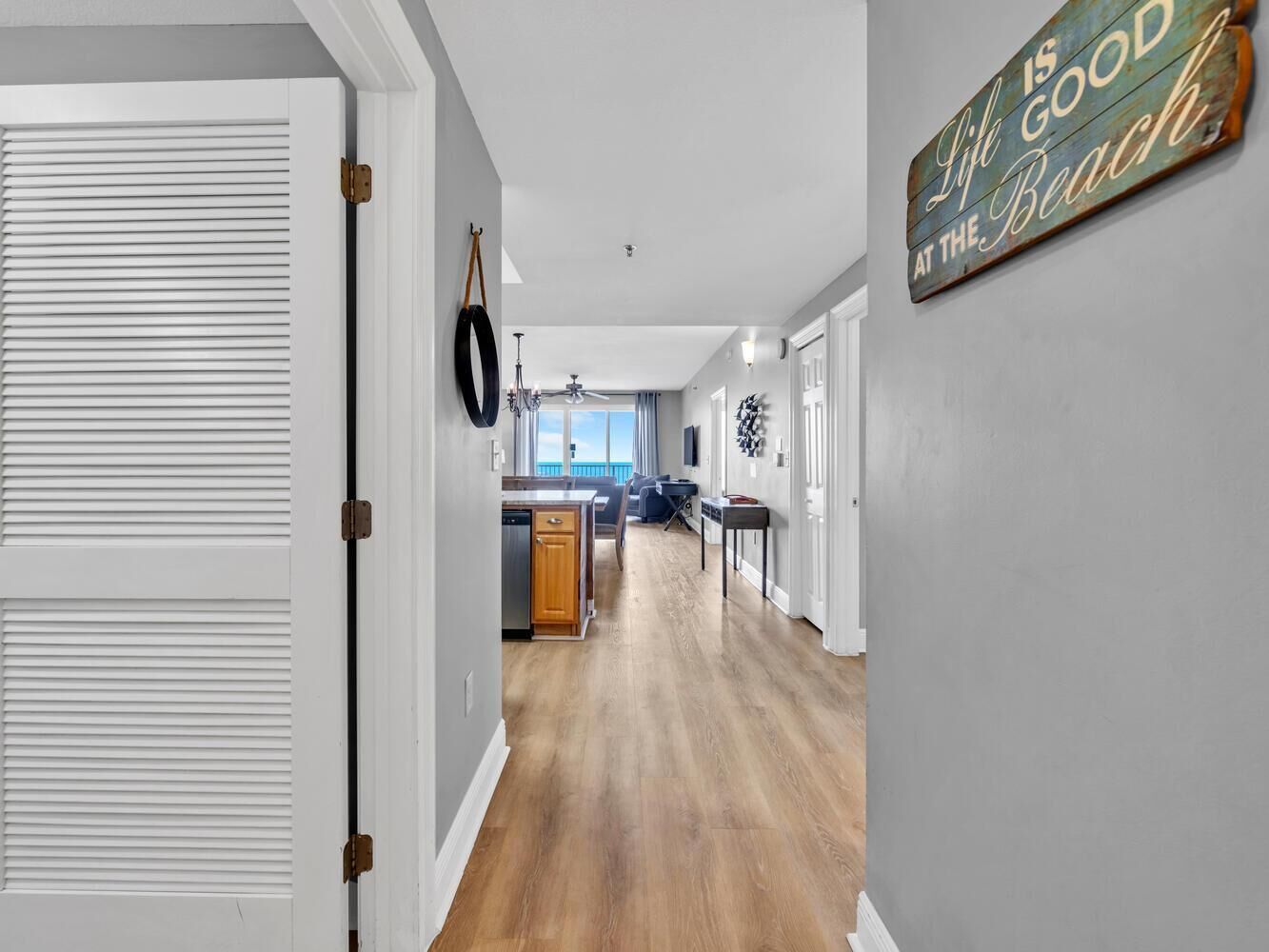 A hallway with a wooden floor, a kitchen area with a dining table, and a sign on the wall.