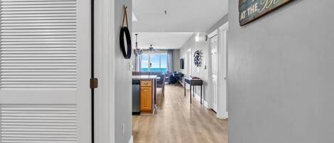 A hallway with a wooden floor, a kitchen area with a dining table, and a sign on the wall.