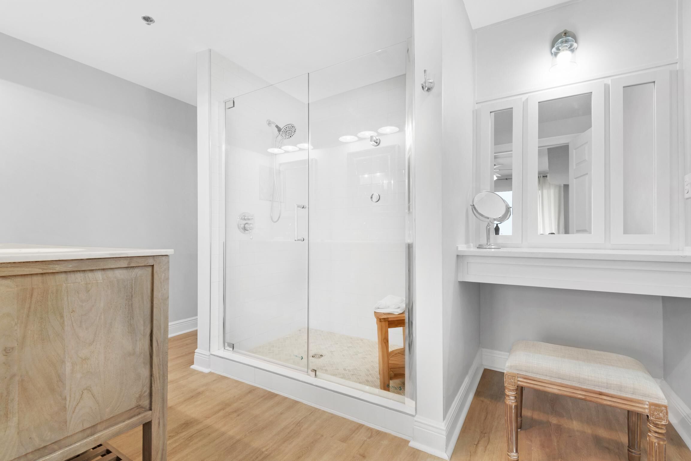 A modern bathroom with a glass-enclosed shower, a wooden bench, and a vanity with a mirror.