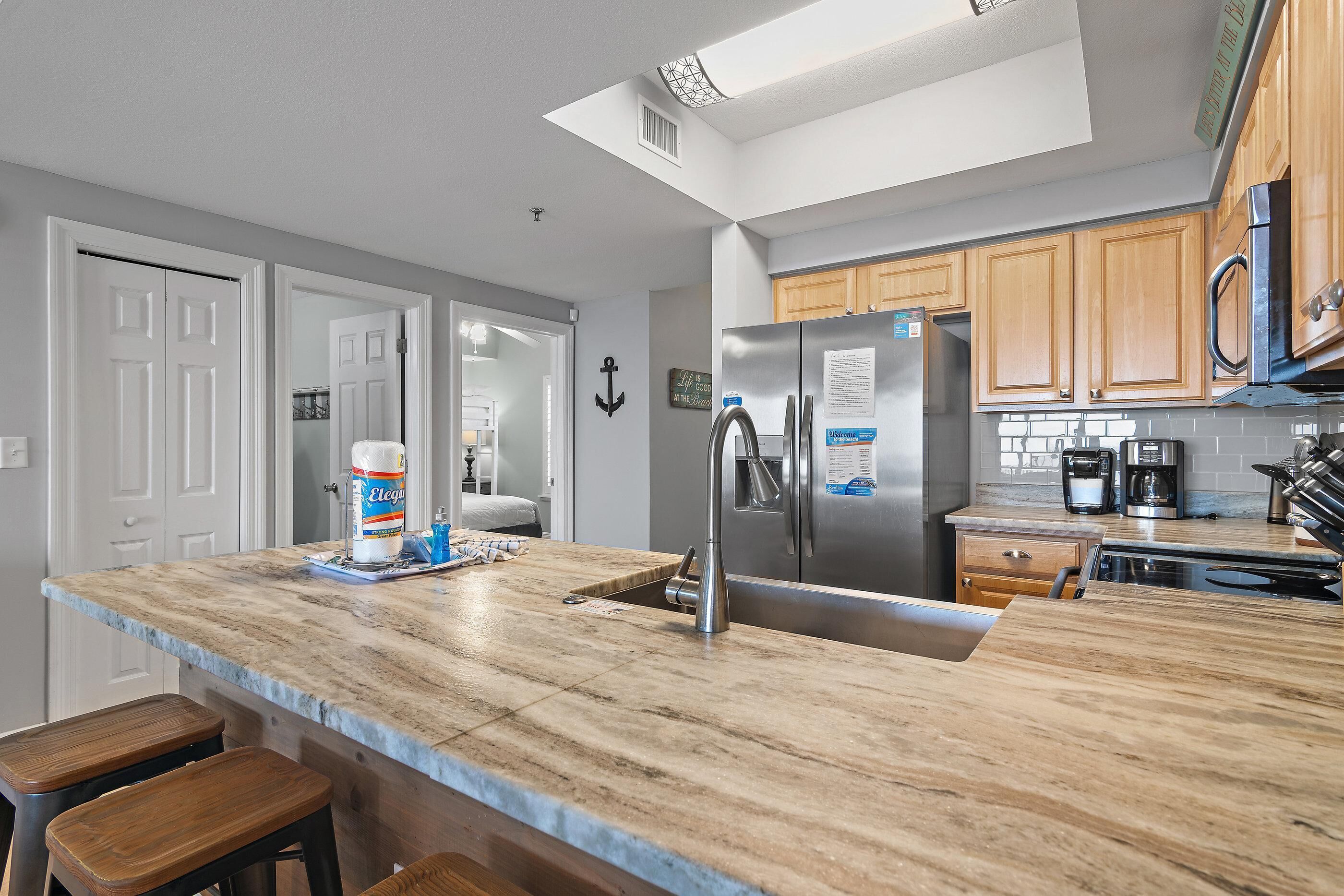 A modern kitchen with a marble countertop, stainless steel appliances, wooden cabinets, and a built-in oven.