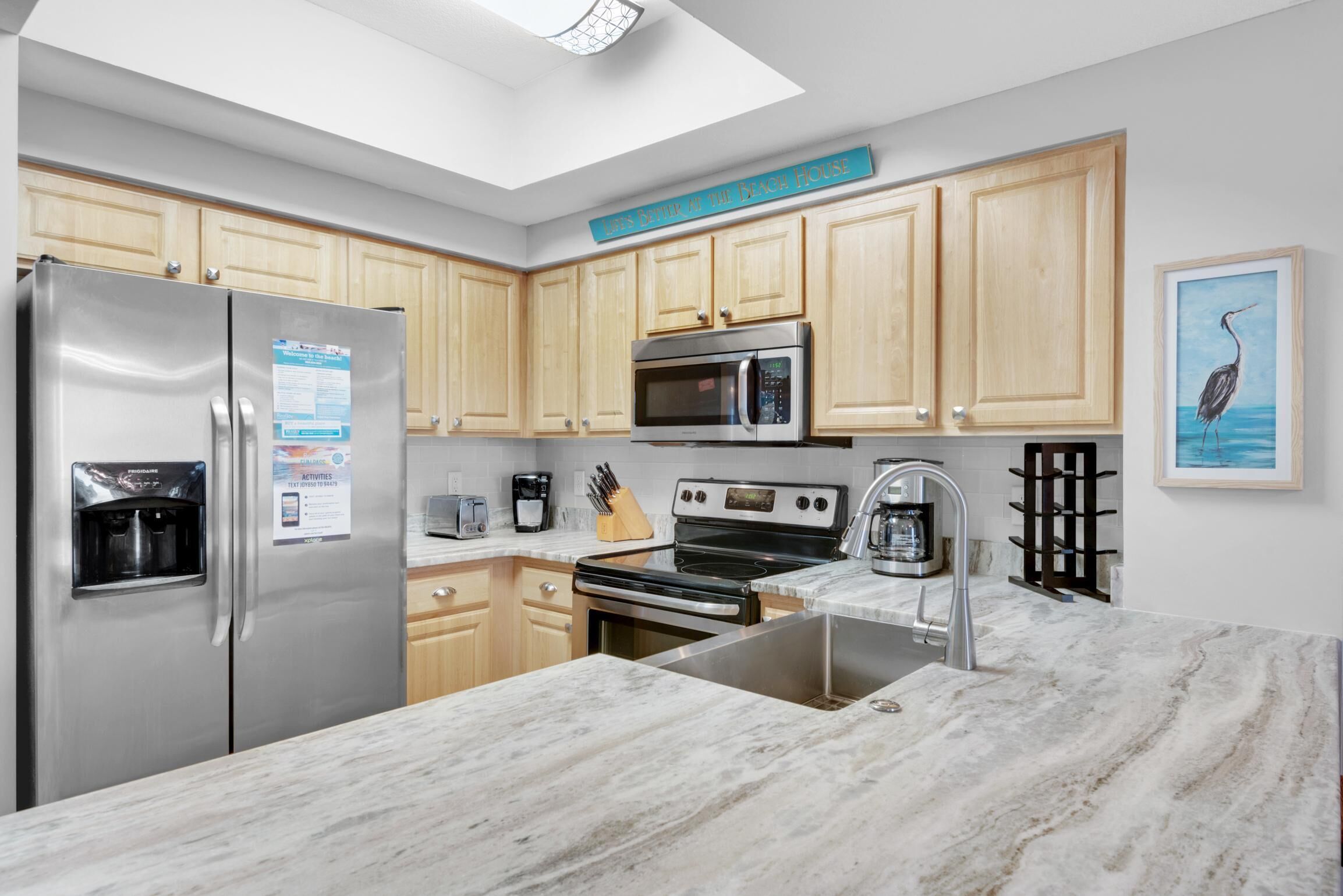 A modern kitchen with wooden cabinets, stainless steel appliances, a marble countertop, and a skylight.