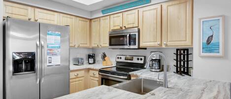 A modern kitchen with wooden cabinets, stainless steel appliances, a marble countertop, and a skylight.