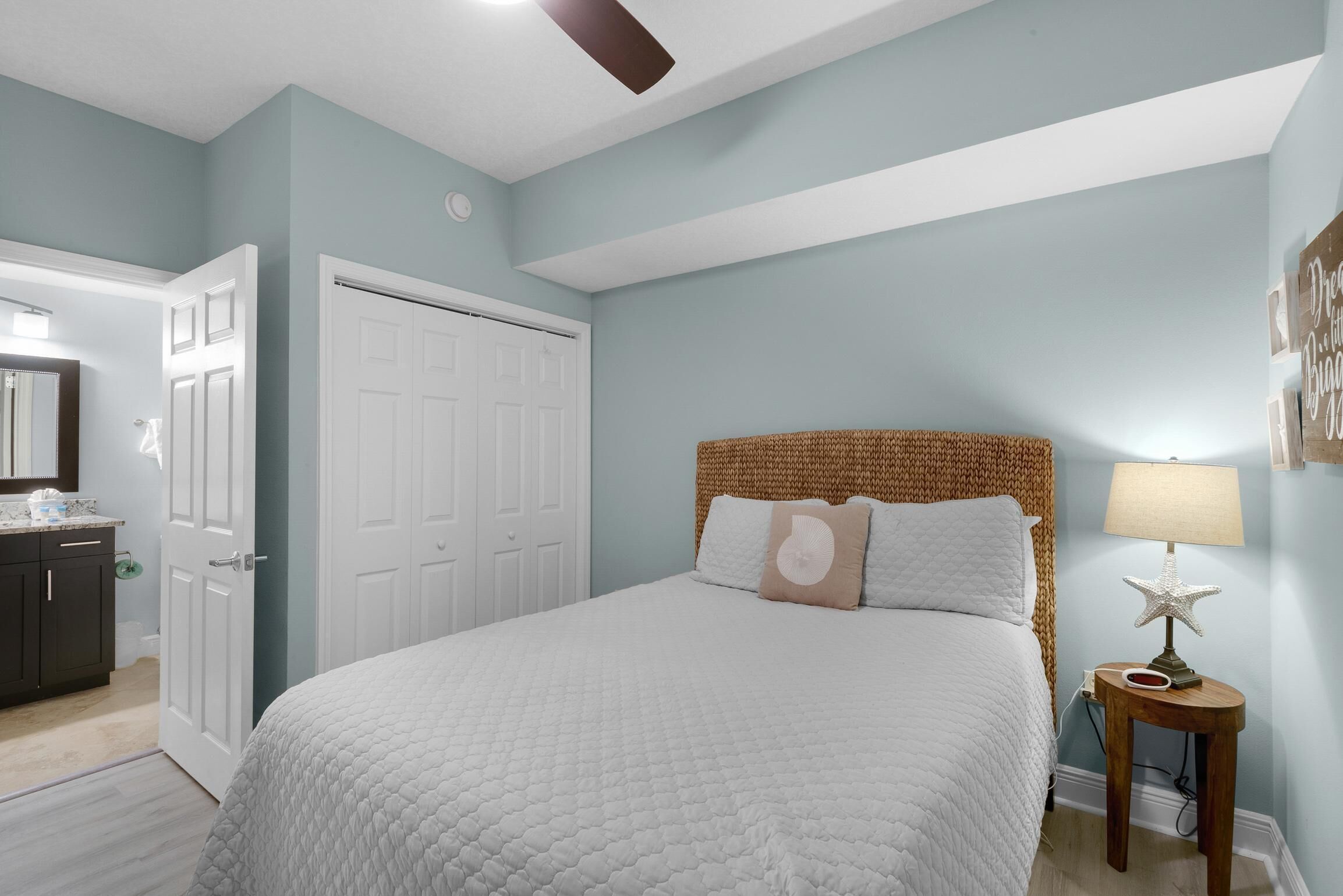 A bedroom with a large bed, a wooden headboard, a bedside table with a lamp, and a door leading to another room.